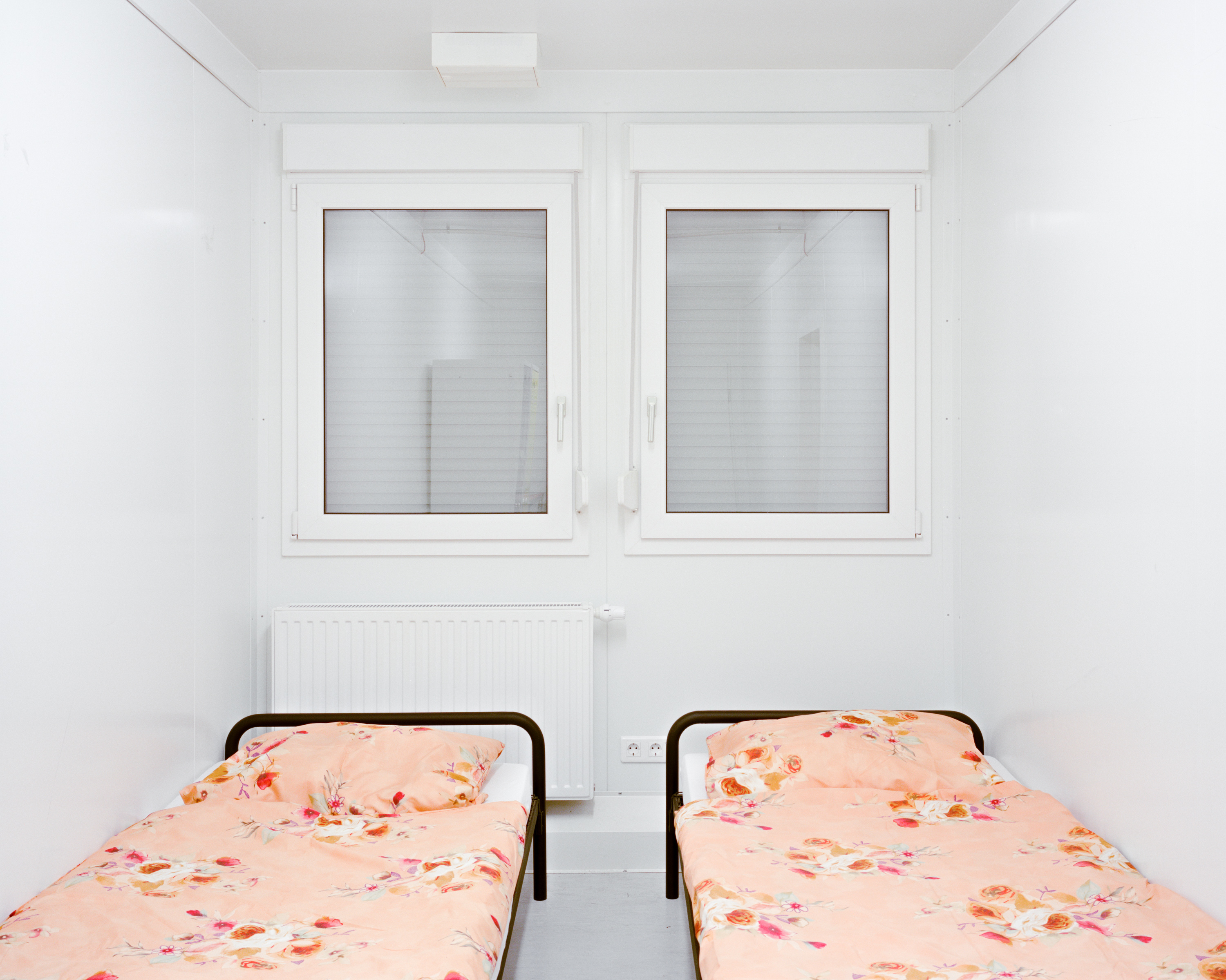 You see two unused single beds in a very small rooms. There is less then a meter space between the beds, the windows are closed. The room is very clean.